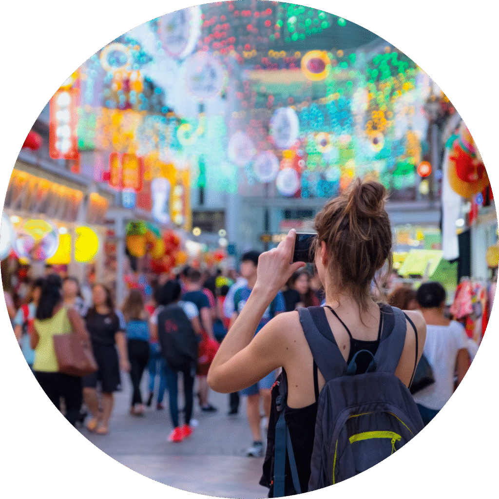 Female tourist capturing vibrant street market scene decorated with colorful lights and lanterns during a festive event