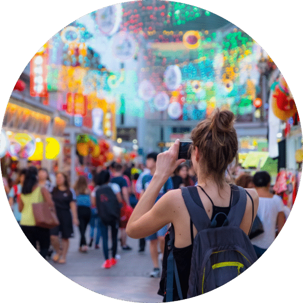 Female tourist capturing vibrant street market scene decorated with colorful lights and lanterns during a festive event